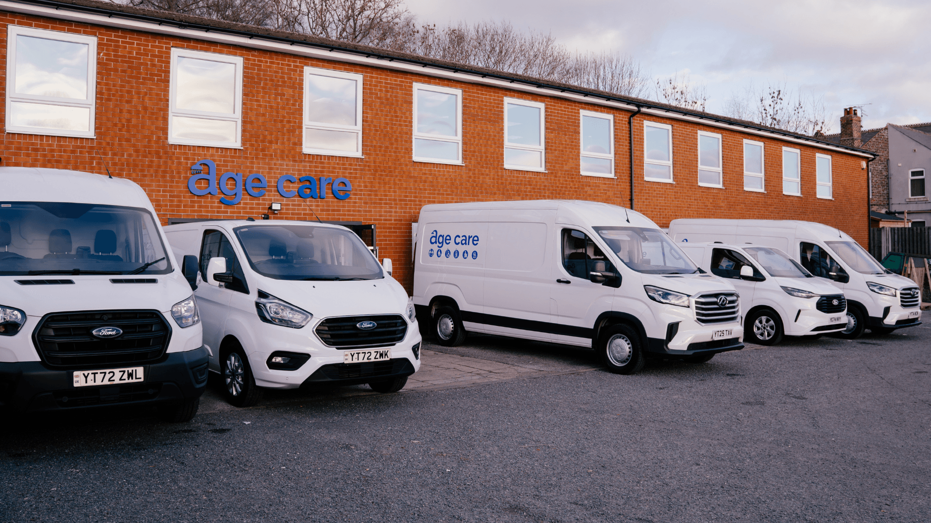 A photo of the exterior of the Age Care Maintenance with several company vans and cars parked outside.